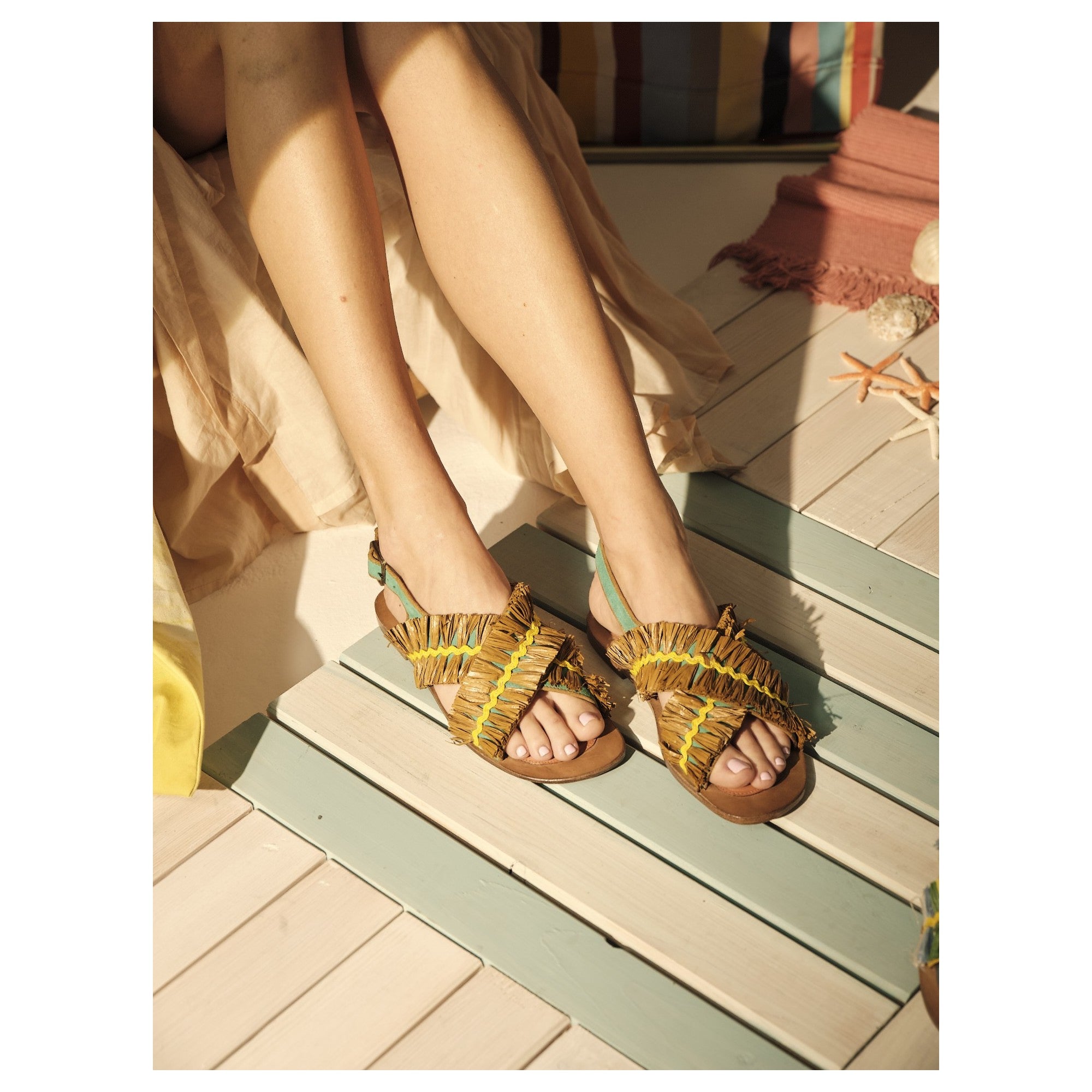 Close-up of Meher Kakalia sandals worn with summer outfit, showing suede turquoise strap and raffia detail.